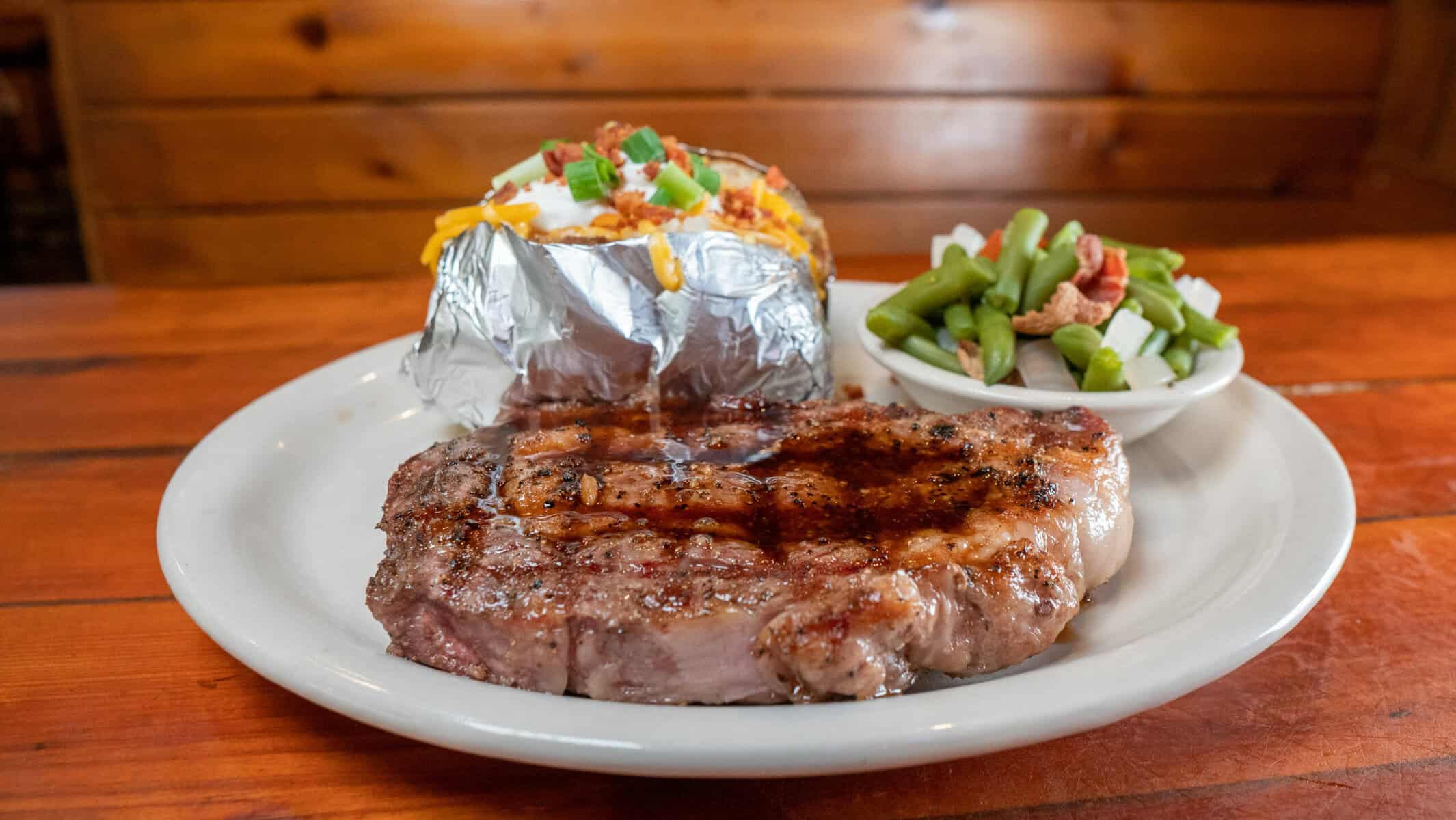 Grill-marked steak with a foil baked potato and side salad at Hofbrau Steaks in Porter, Texas