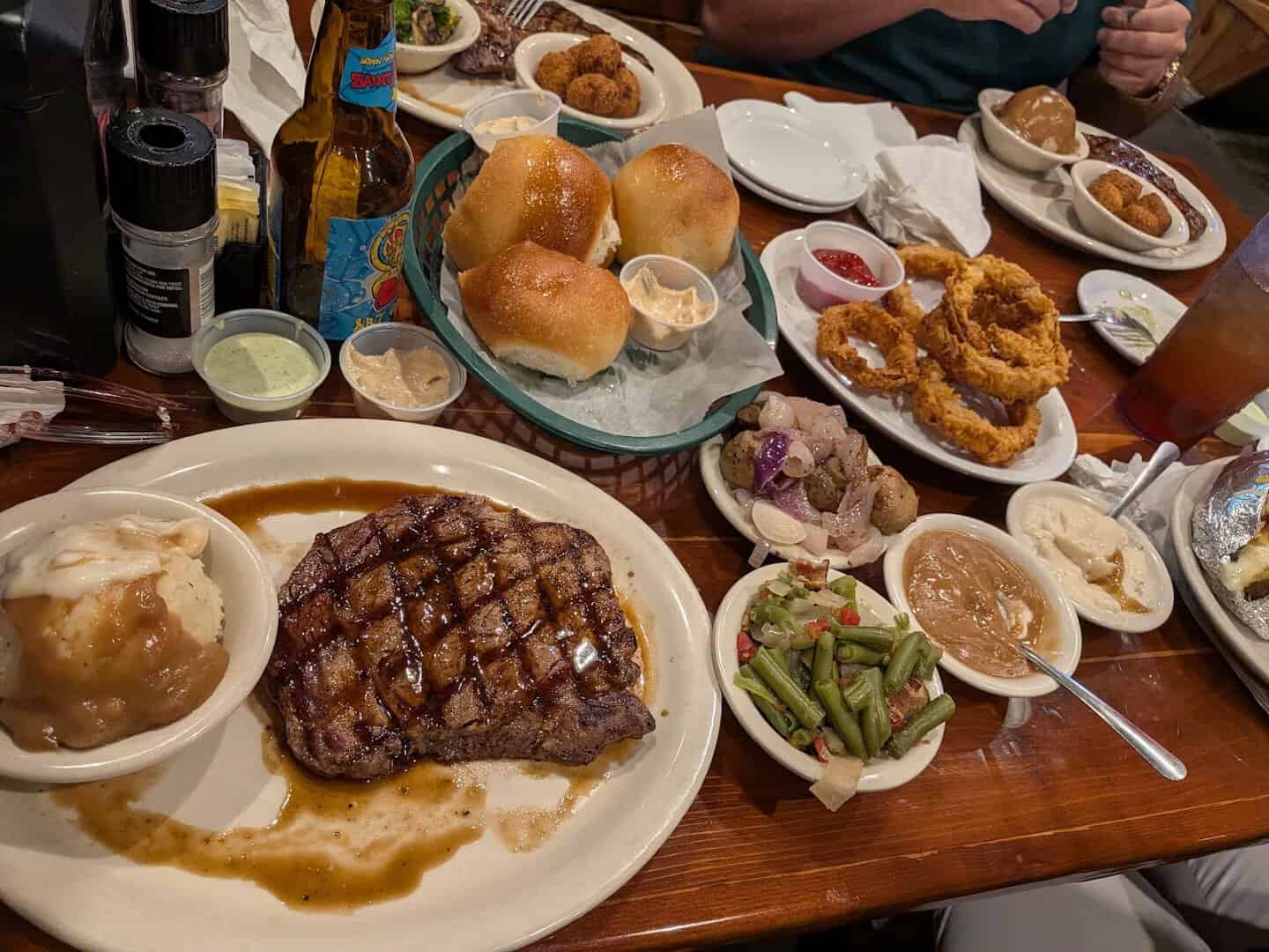 Table spread of steak, rolls, onion rings and sides at Hofbrau Steaks in Porter, Texas
