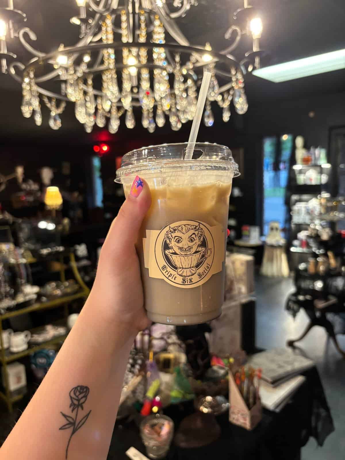 Iced latte held beneath a crystal chandelier at Triple Six Social in San Marcos
