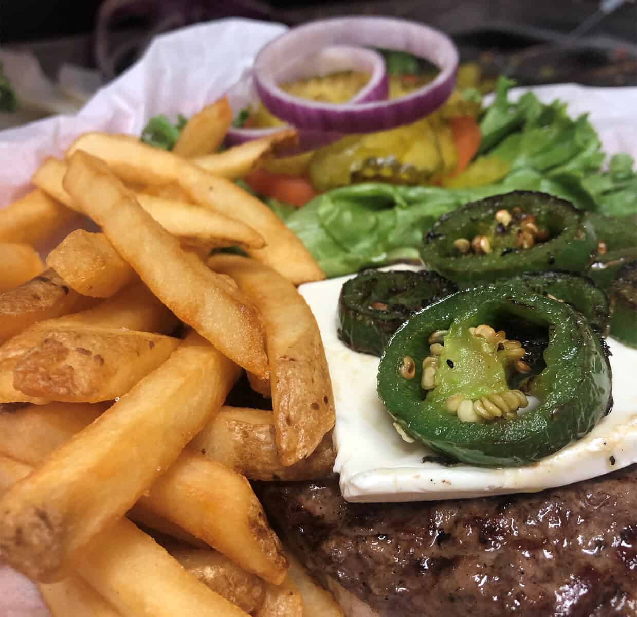 Jalapeno cream cheese burger with roasted jalapenos and a pile of fries at Roadhouse in Bastrop, Texas