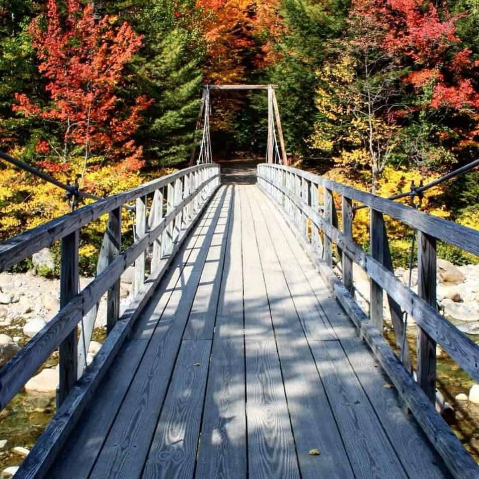 Footbridge over a river framed by red and orange autumn foliage on the Kancamagus Highway, New Hampshire