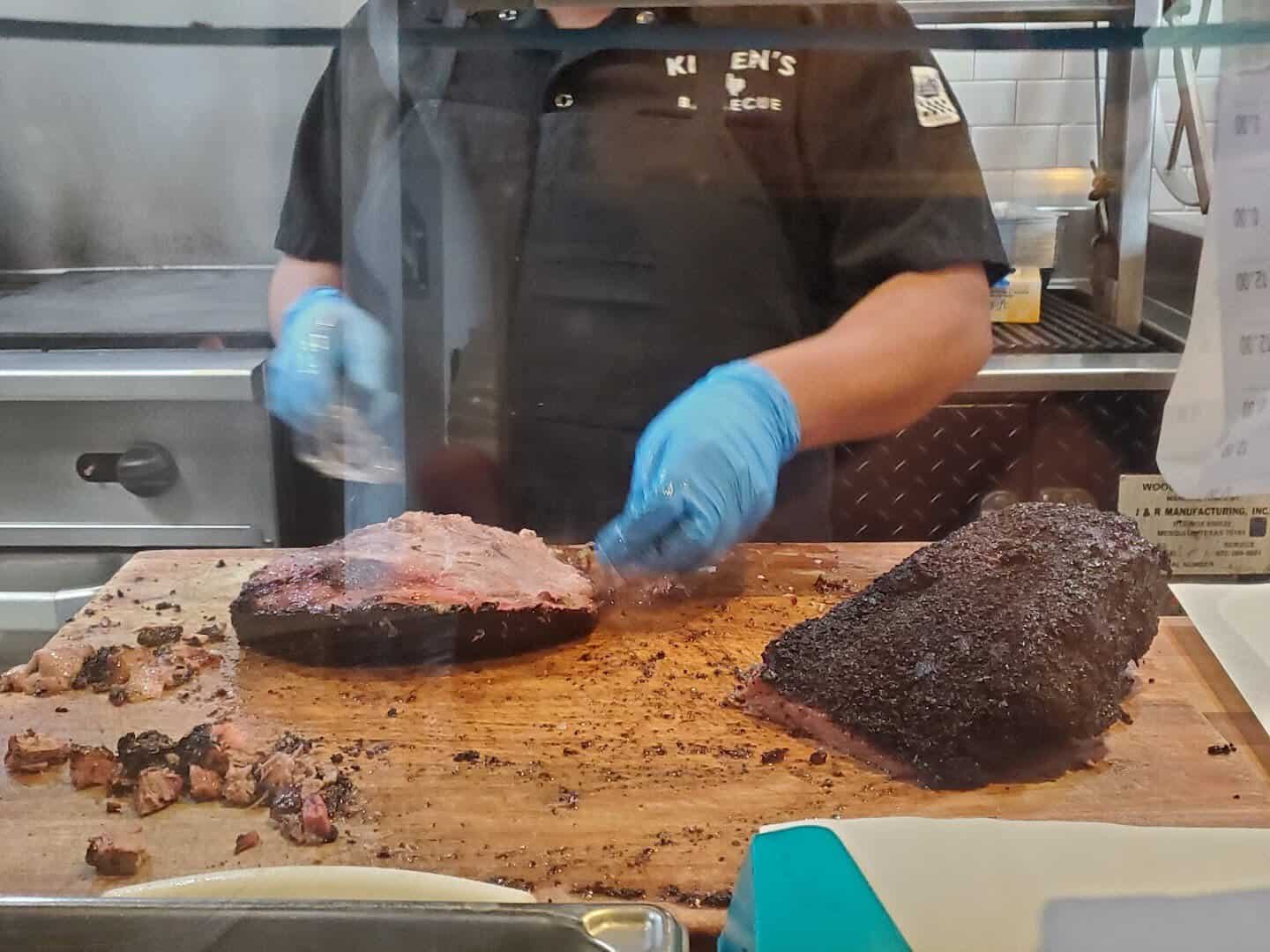 Gloved hands slicing smoked brisket at the pass at Killen's Barbecue in Pearland, Texas