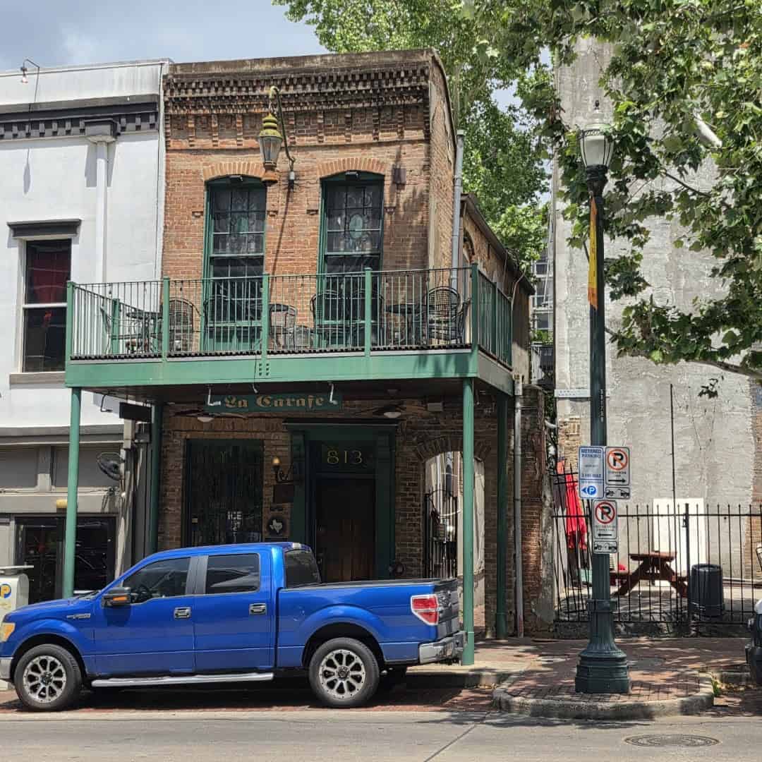 Historic brick building housing La Carafe bar with green balcony in downtown Houston
