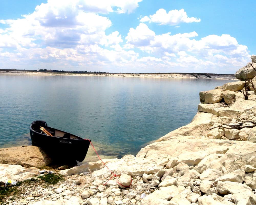 A canoe resting on the rocky blue shoreline of Lake Amistad, Texas