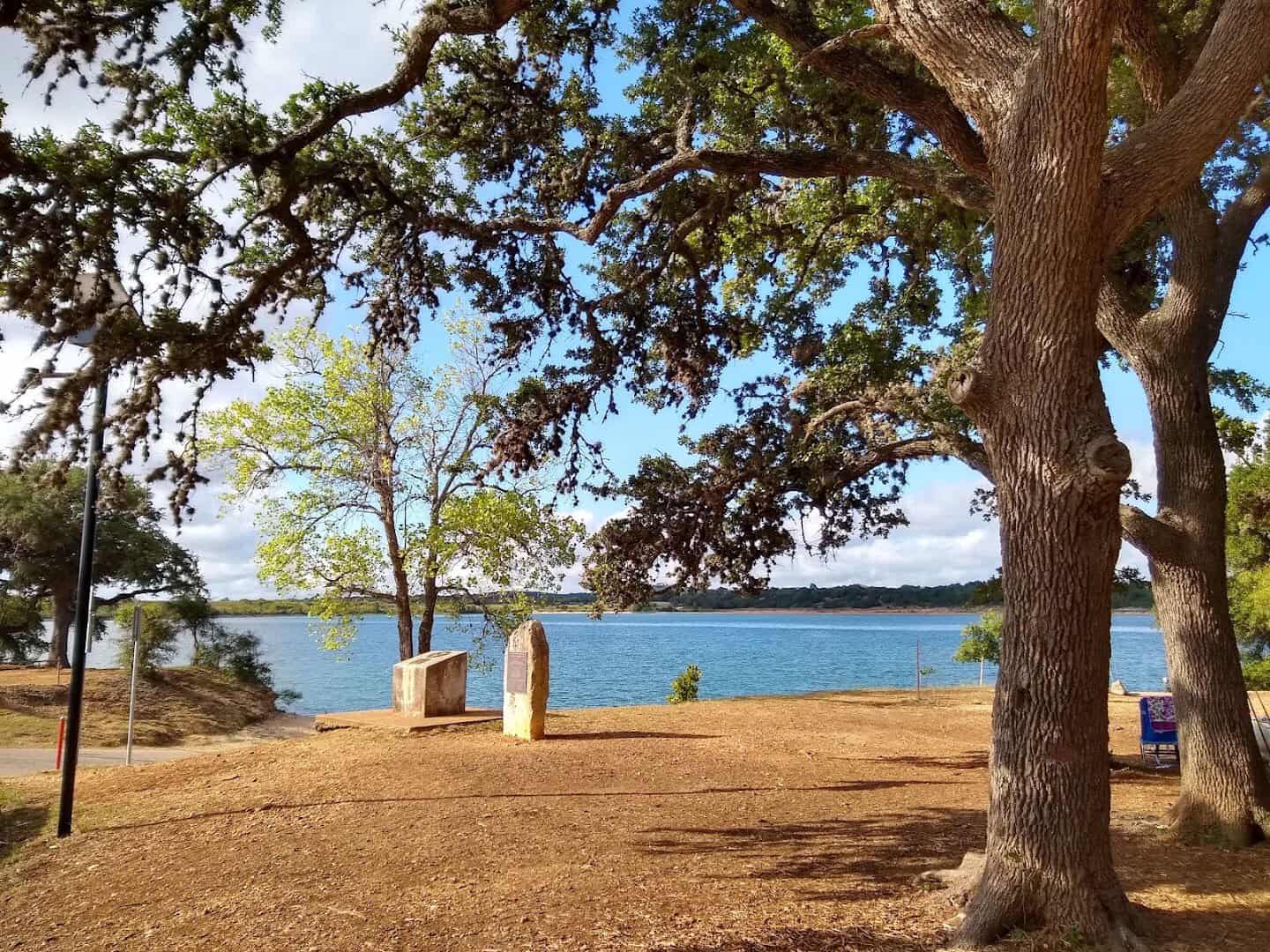 Live oaks shading the gravel shoreline above the turquoise water of Boerne City Lake