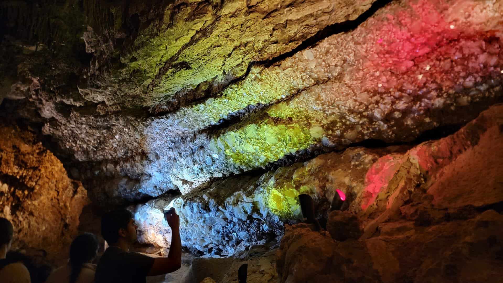 Crystal-lined cavern wall glowing red and green under ultraviolet light on the blacklight tour at Longhorn Cavern