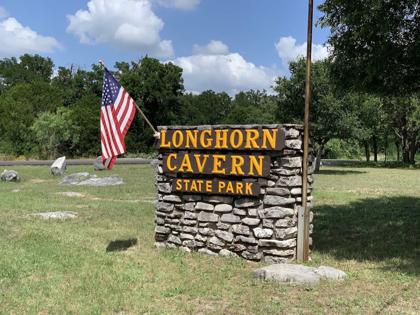 Stone entrance sign for Longhorn Cavern State Park with a Texas roadside flag in Burnet, Texas