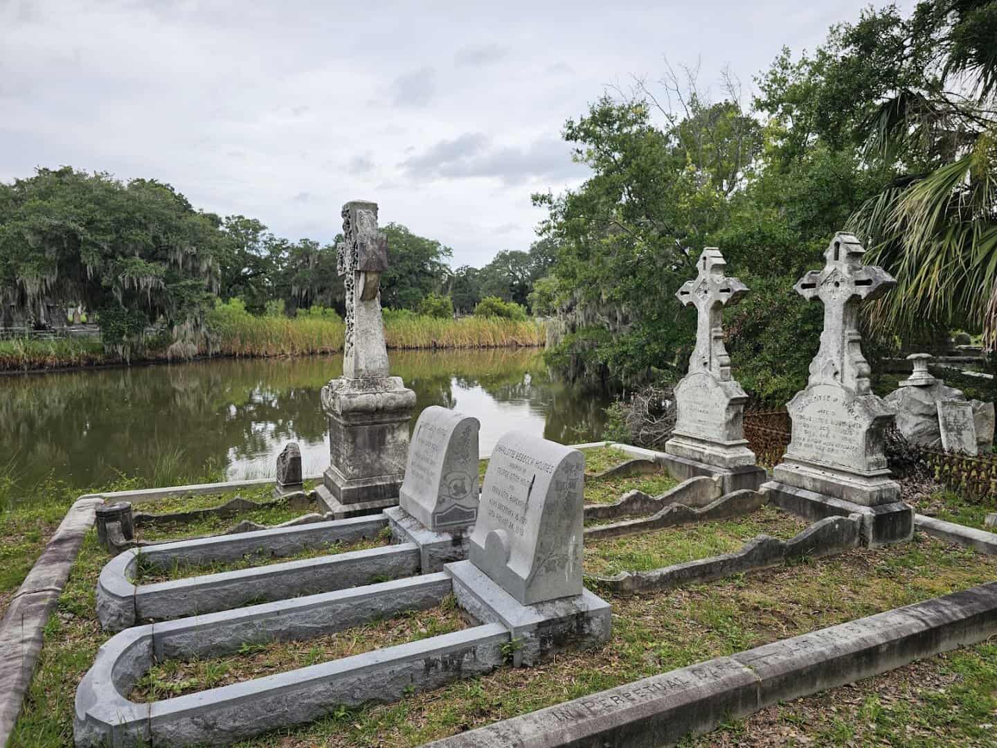 Graves and crosses beside a lagoon under moss-draped live oaks at Magnolia Cemetery in Charleston, South Carolina