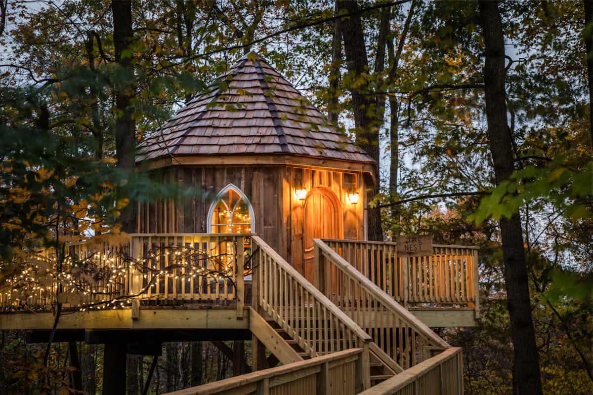 Lit treehouse among autumn trees at The Mohicans Treehouse Resort in Glenmont, Ohio