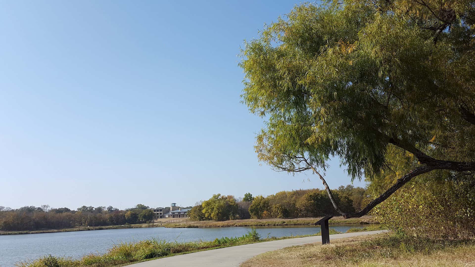 A paved trail curving alongside the water at Oak Point Park and Nature Preserve in Plano, Texas