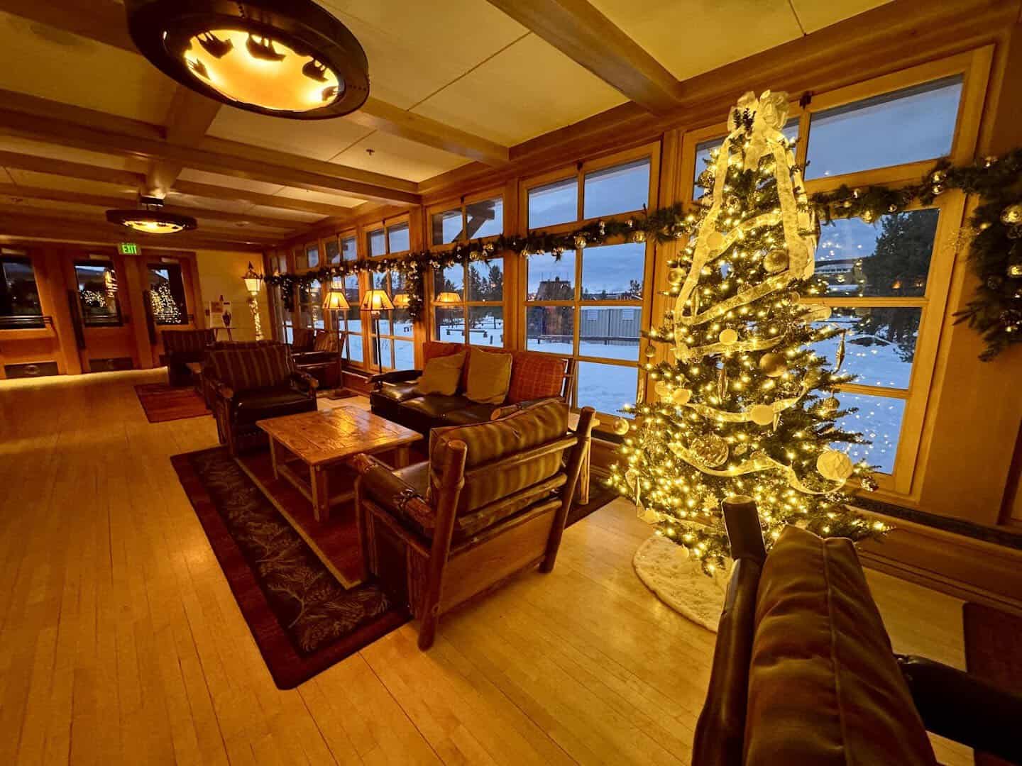 Lodge lounge with lit tree and snow outside at Old Faithful Snow Lodge, Yellowstone, Wyoming