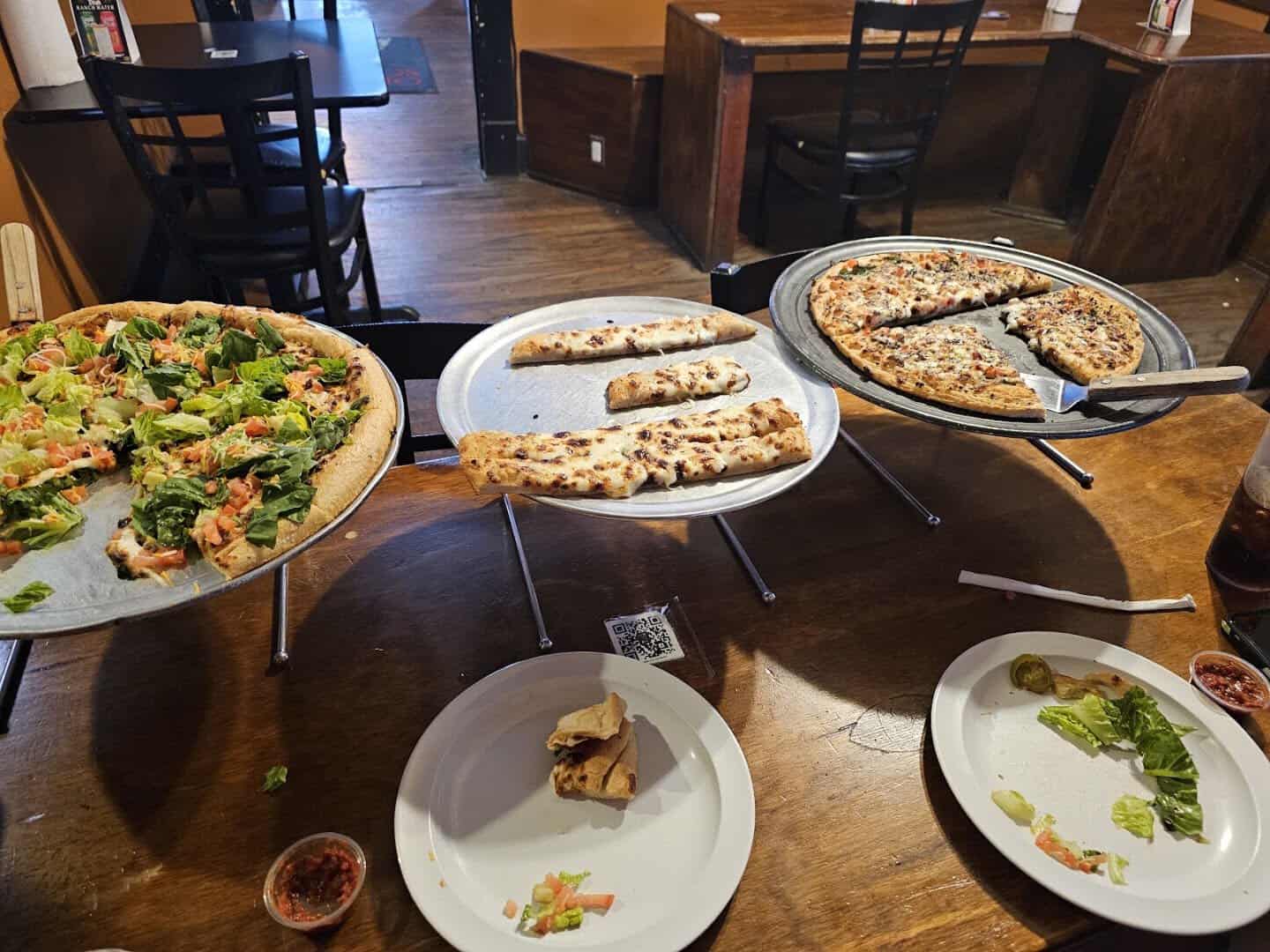 A spread of pizzas and plates at Old School Pizza Tavern in Arlington, Texas