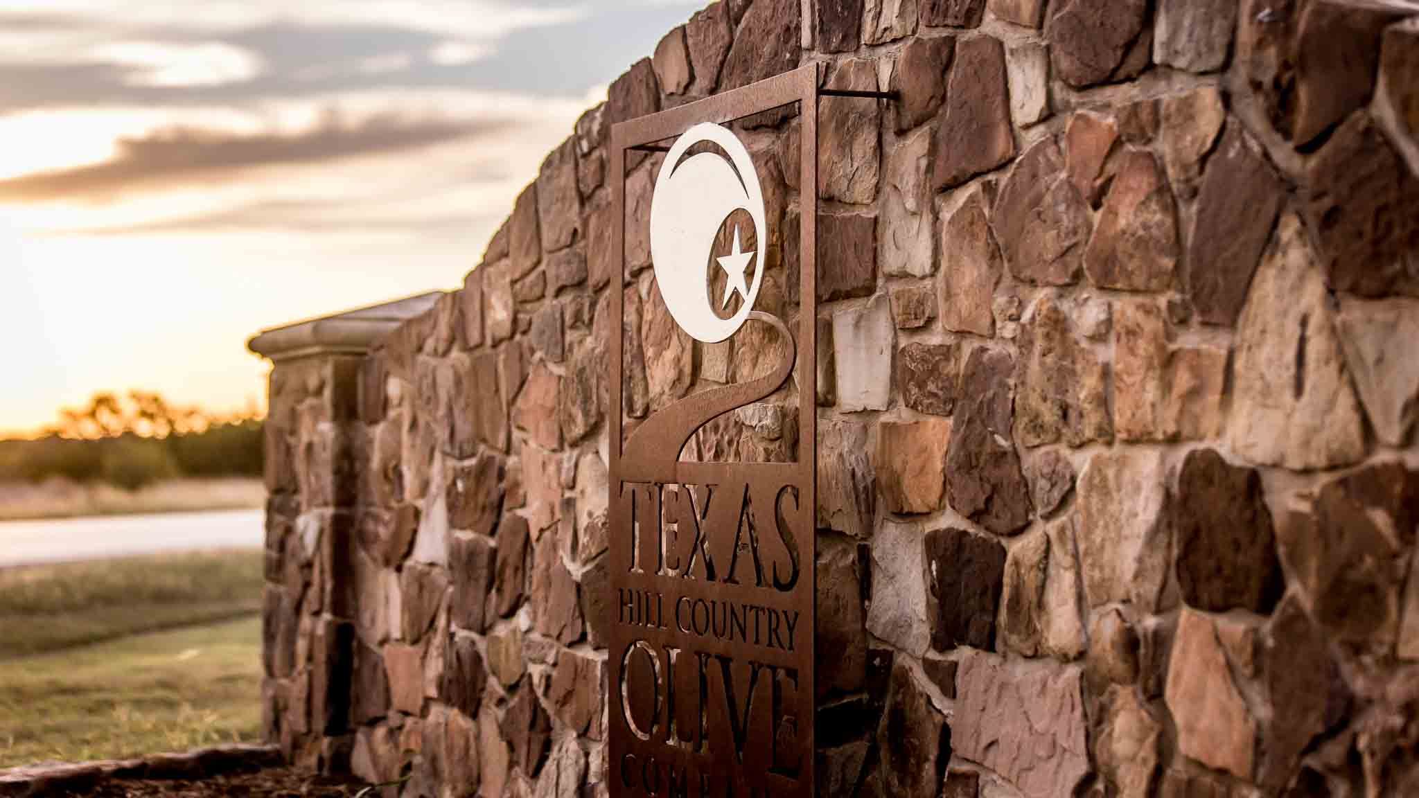 Stone entrance sign at Texas Hill Country Olive Co. at sunset in Dripping Springs, Texas