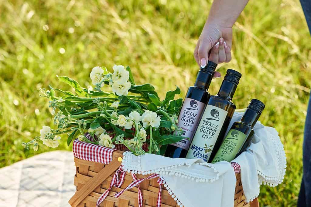 Texas Hill Country olive oil bottles in a basket in a grassy Hill Country field