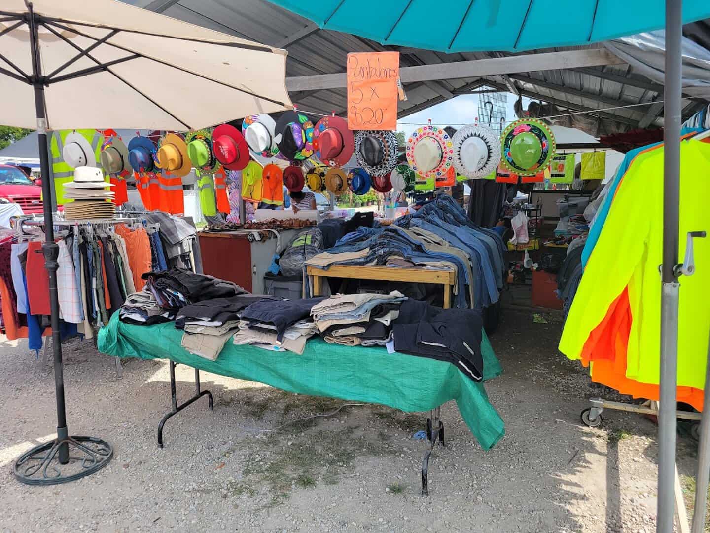 Clothing and workwear laid out on outdoor tables under an umbrella at Cole's flea market in Pearland, Texas