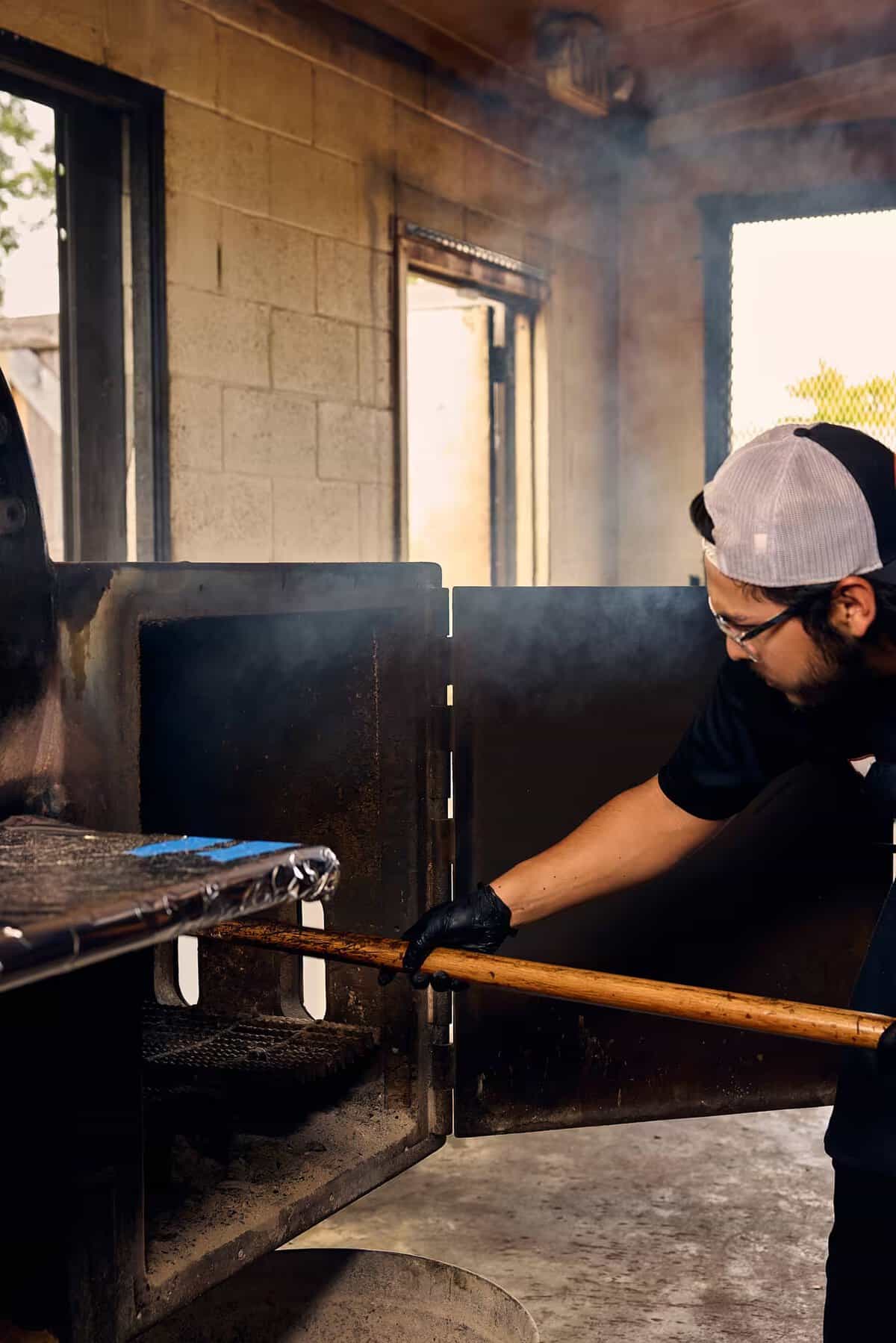 Pitmaster working the offset smoker in billowing smoke at Pinkerton's Barbecue