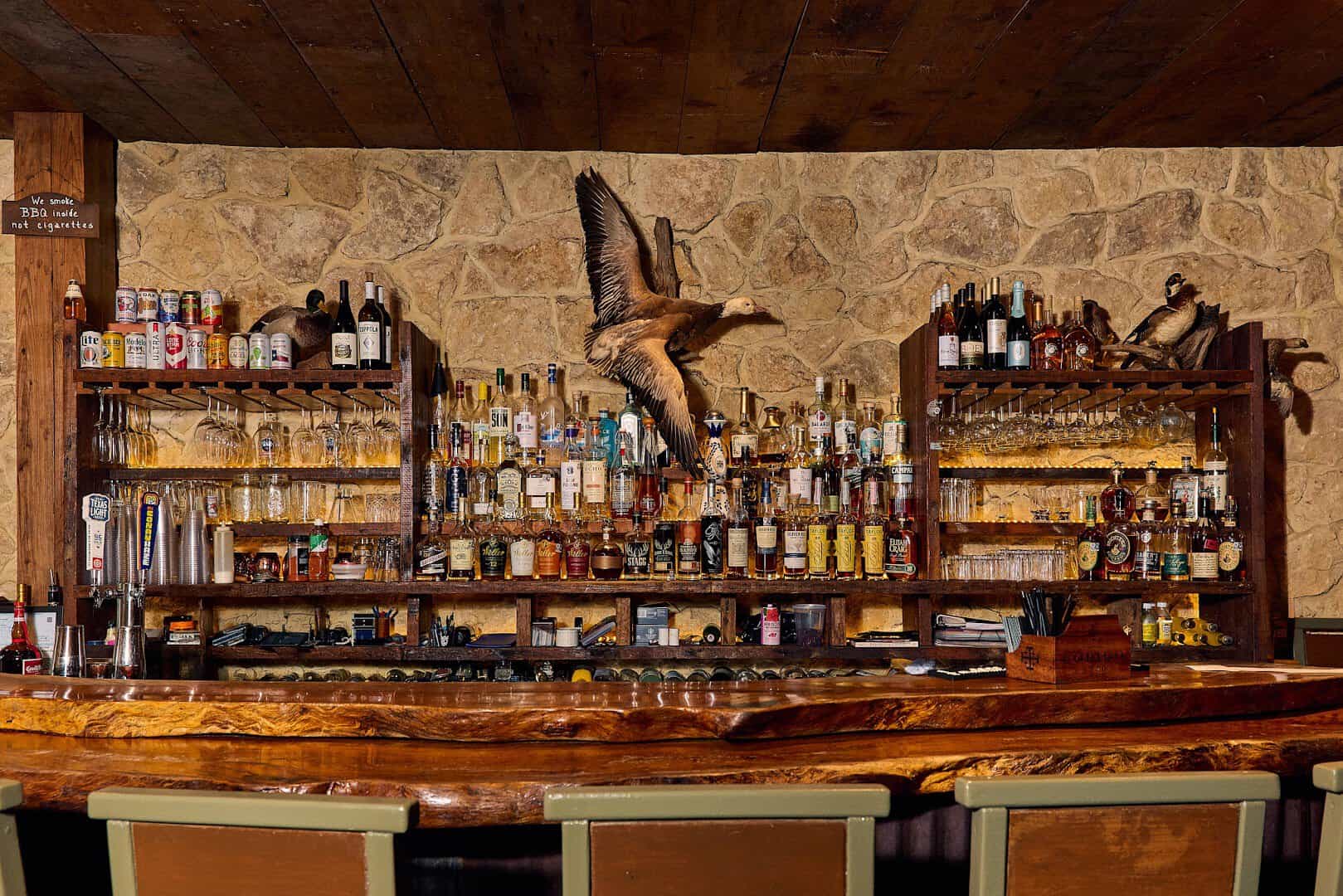 Rustic bar with stone wall and mounts at Pinkerton's Barbecue in Houston