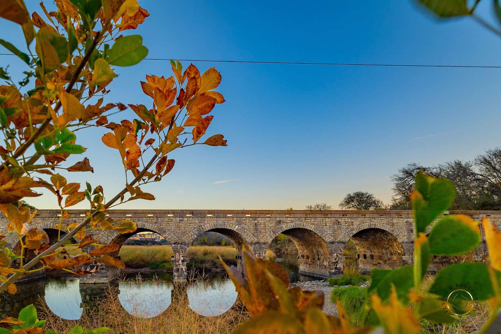 The Possum Kingdom Stone Arch Bridge framed by autumn leaves over the Brazos River
