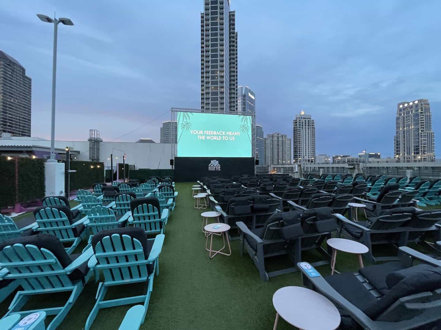 Rows of teal Adirondack chairs facing the screen with the Houston skyline at Rooftop Cinema Club Uptown