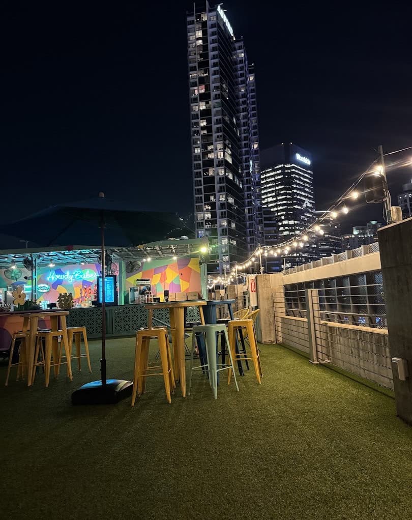 Rooftop bar with high tables and stools lit at night with a Houston tower behind at Rooftop Cinema Club Uptown