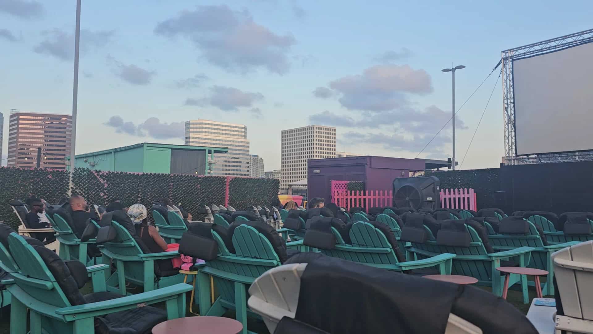Teal Adirondack chairs facing the outdoor screen at dusk at Rooftop Cinema Club Uptown in Houston