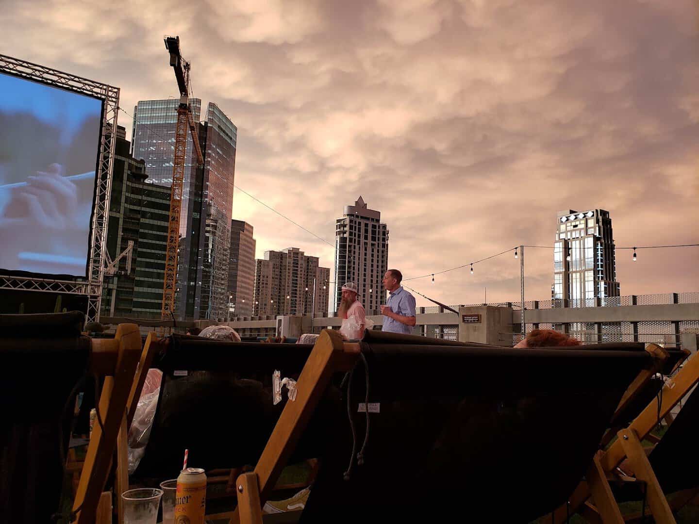 Outdoor movie screen and the Houston skyline under a dramatic dusk sky at Rooftop Cinema Club Uptown