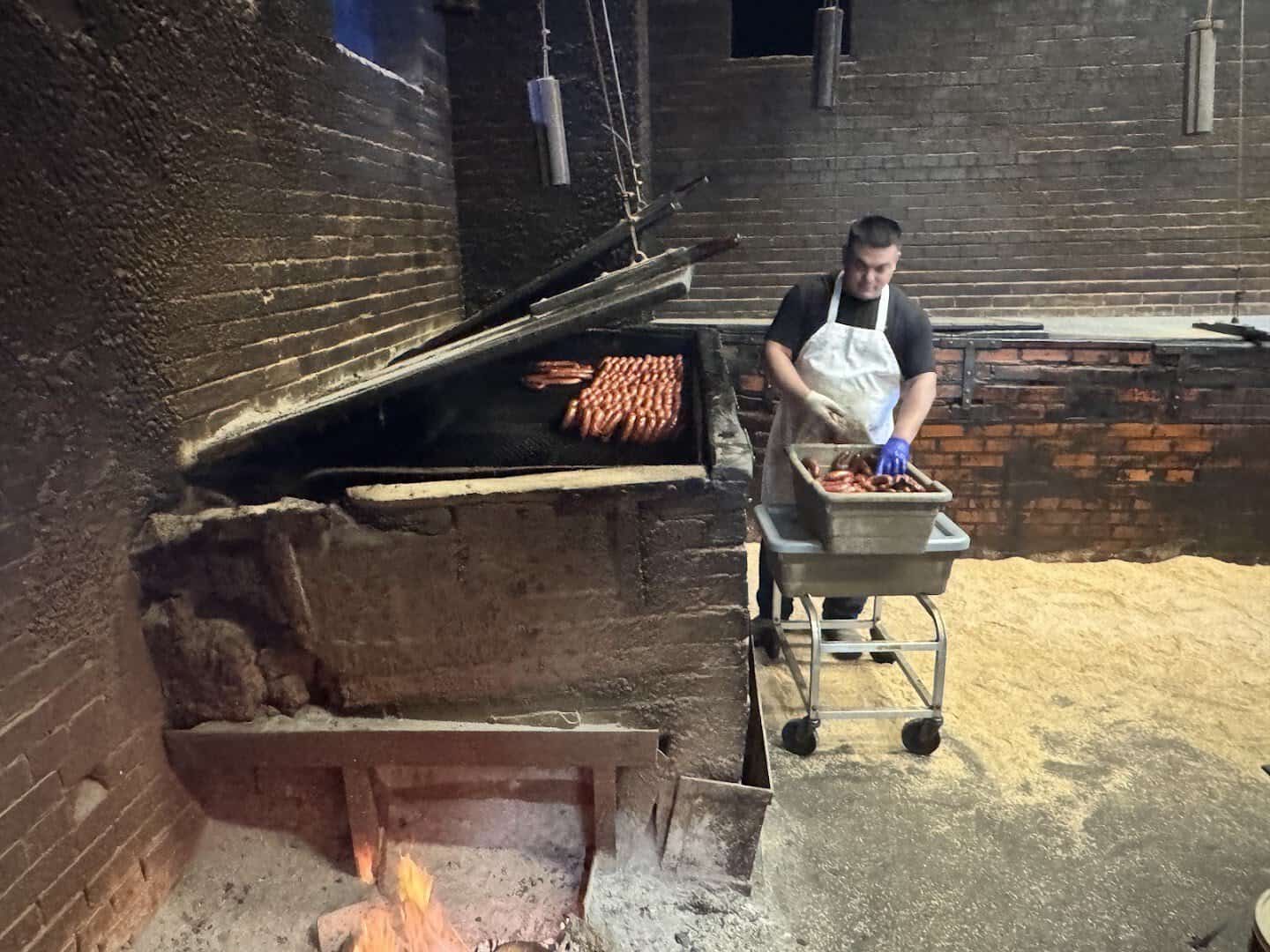 Pitmaster slicing brisket beside the open floor-level fire pit at Smitty's Market in Lockhart, Texas