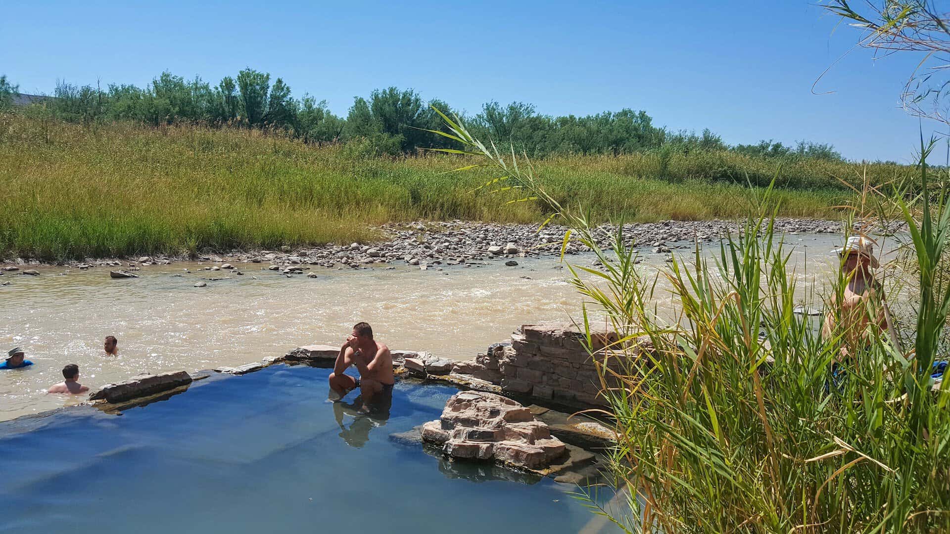 Visitors soaking in the warm mineral pool at Big Bend Hot Springs beside the river
