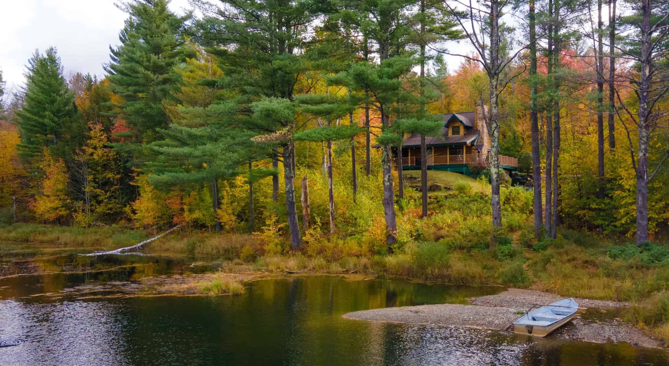 Log cabins beside a pond in autumn foliage at Sterling Ridge Resort in Vermont's Green Mountains