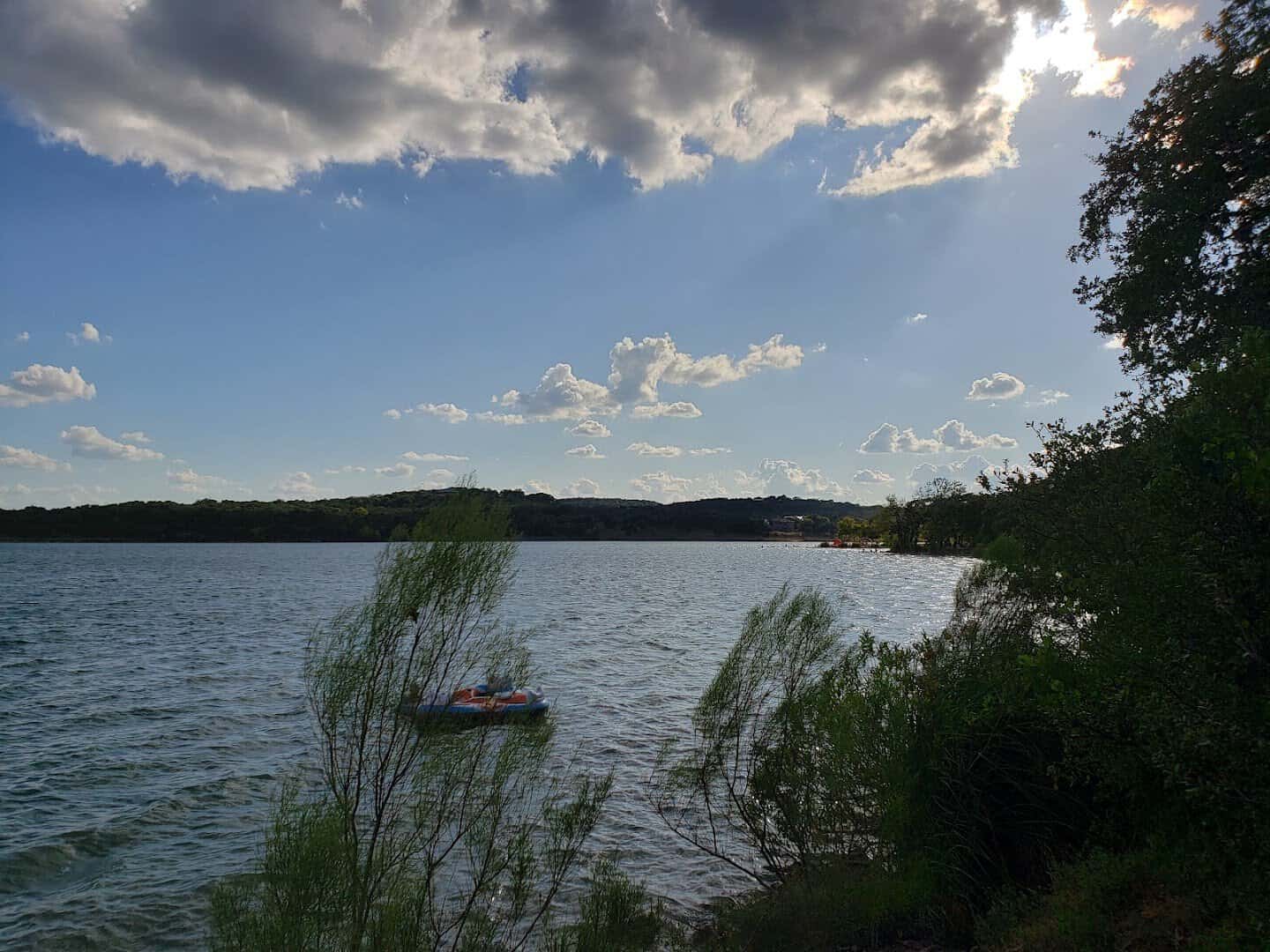 Big clouds building over Boerne City Lake with a small paddle boat on the water