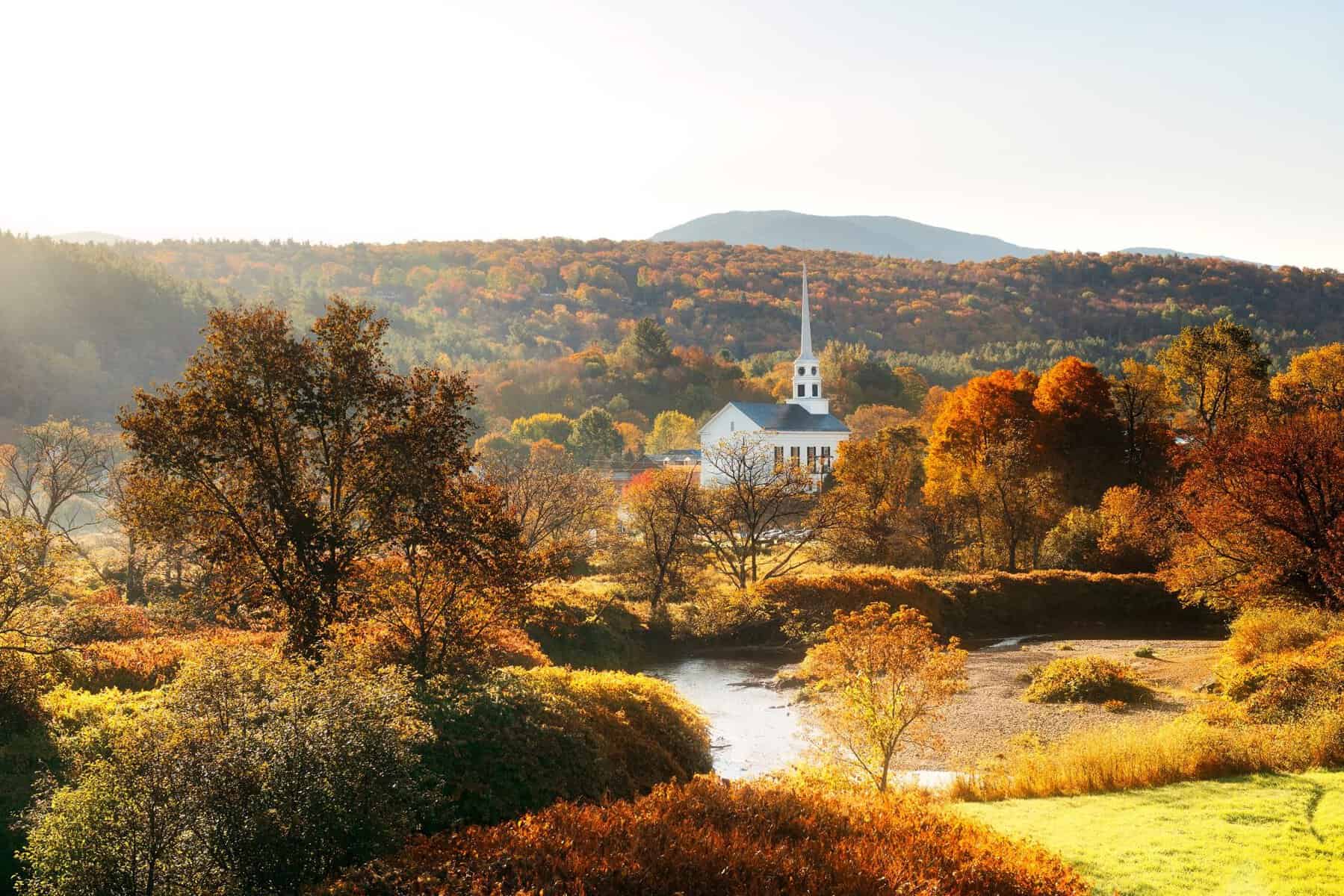 The white Stowe Community Church steeple amid fall foliage in Stowe, Vermont