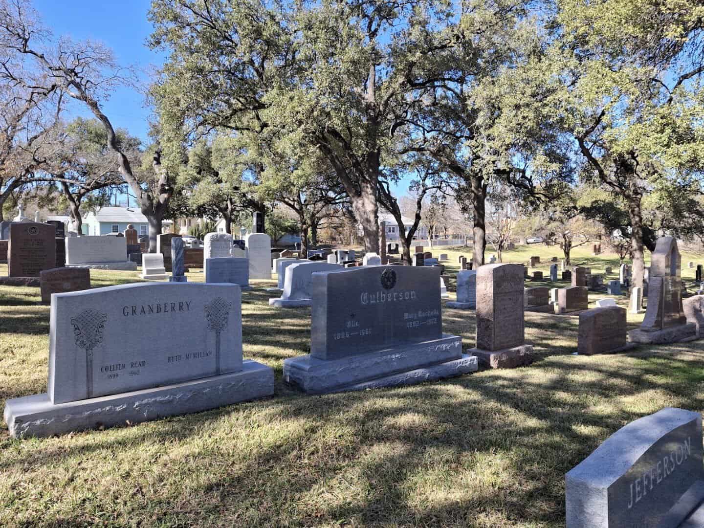 Historic gravestones on green slopes shaded by live oaks at the Texas State Cemetery in Austin, Texas