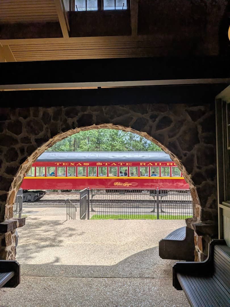 A stone archway framing a Texas State Railroad train at the depot