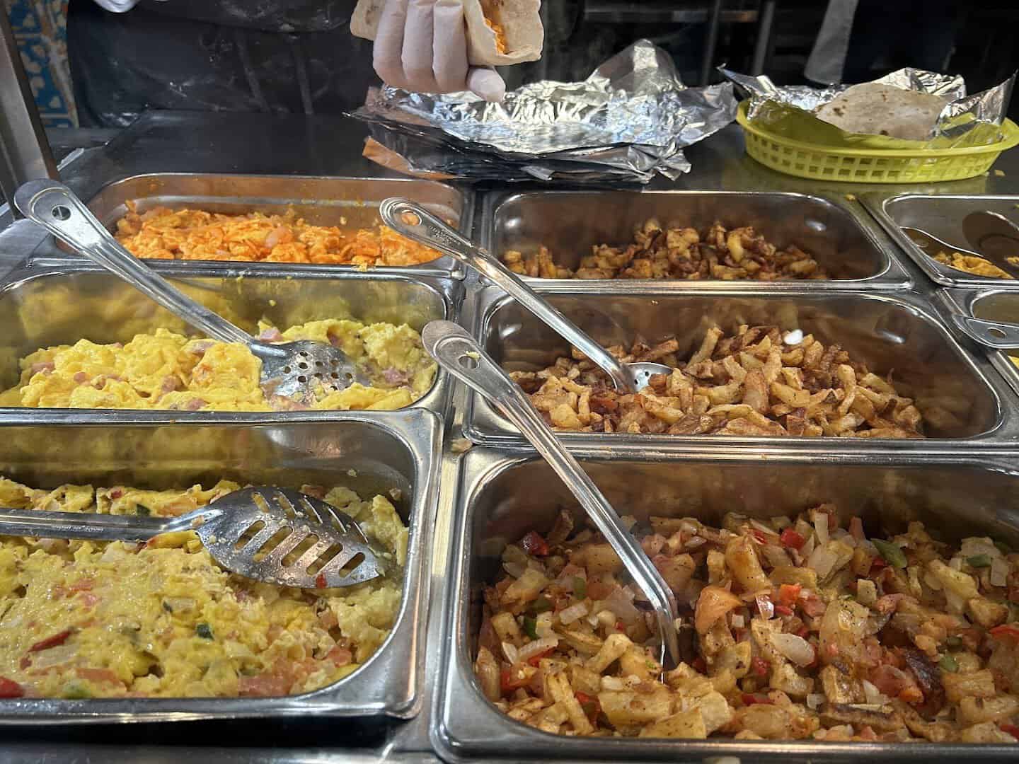 Trays of barbacoa, egg, and potato fillings at Titas Taco House in Humble, Texas