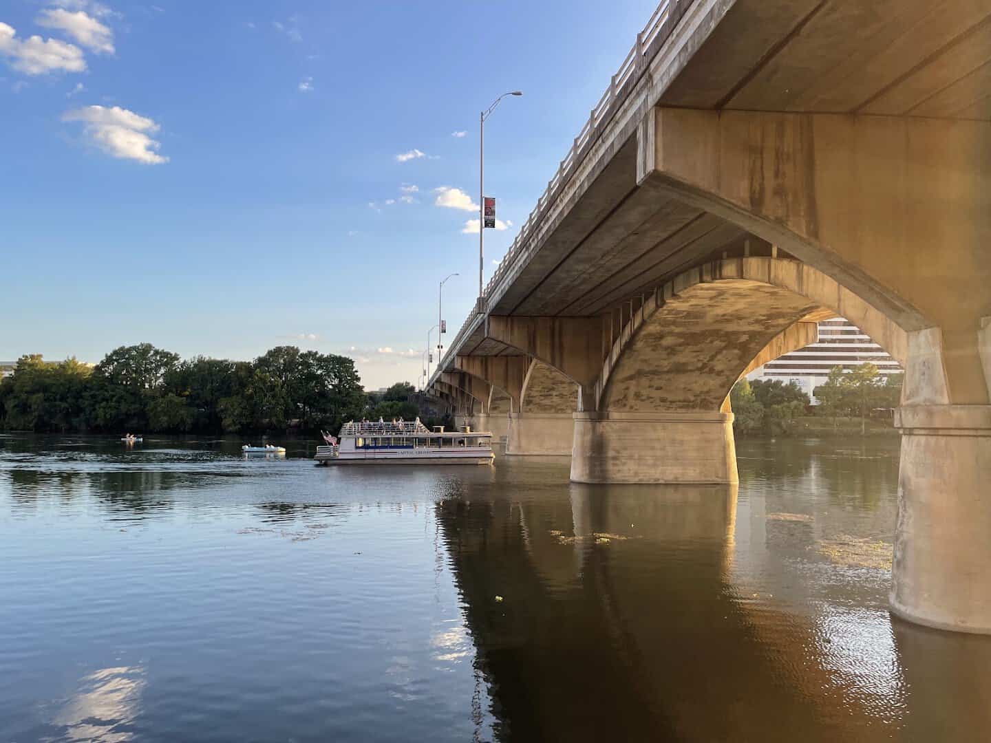A tour boat passing under the Congress Avenue Bridge in Austin on a bright afternoon