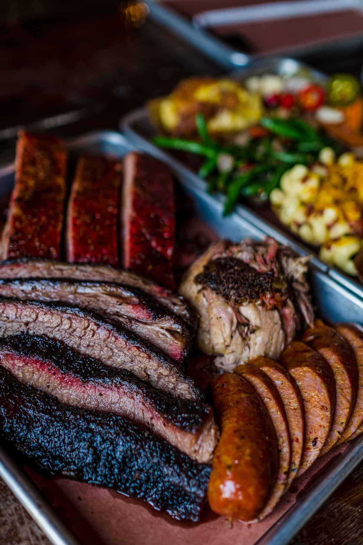 Sliced brisket, ribs and sausage with sides at Truth BBQ in Houston, Texas