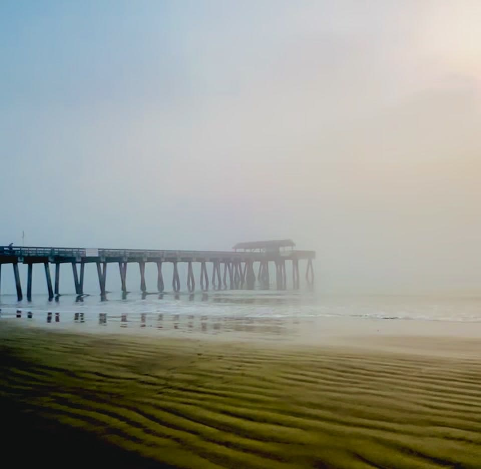 A fishing pier reaching into the fog over the sand at Tybee Island, Georgia
