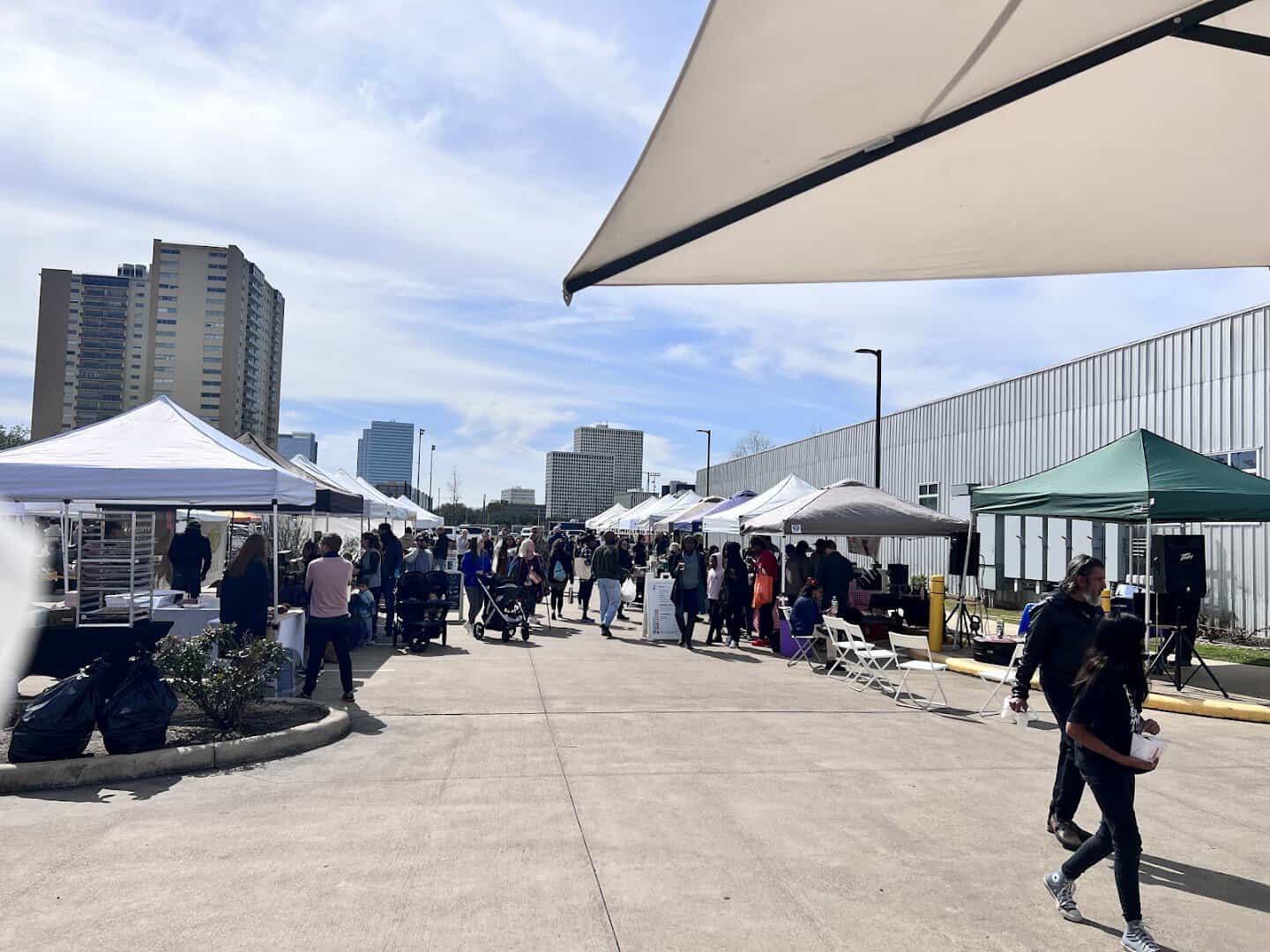 Vendor tents lining the walkway at Urban Harvest Farmers Market with the Houston skyline behind