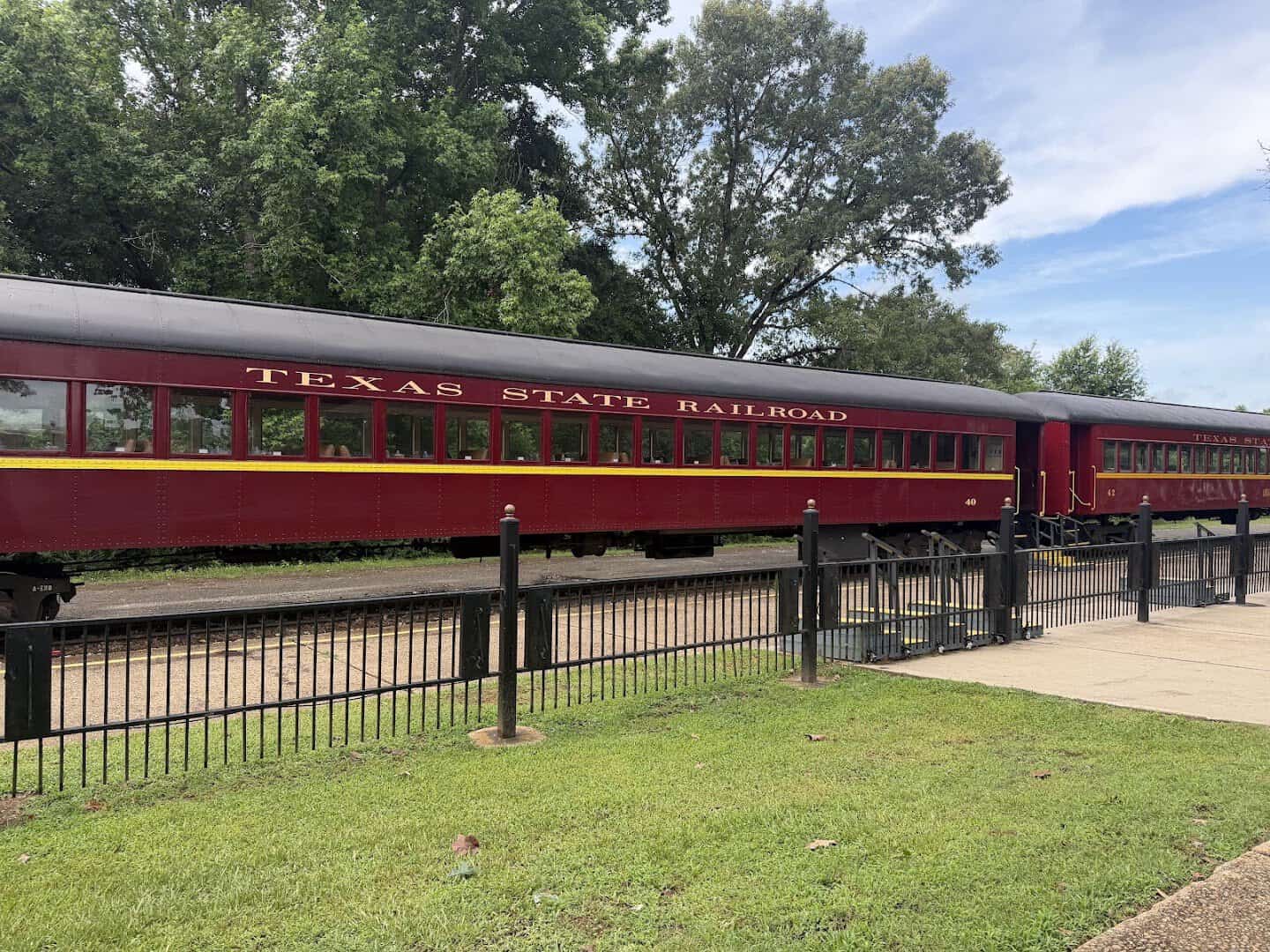 Vintage maroon coaches lettered Texas State Railroad at the depot