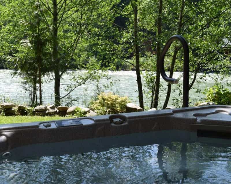 Covered hot tub with river and forest views at Whispering Waters cabin in Baring, Washington