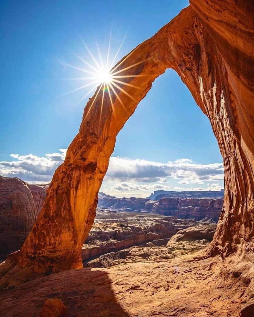Sunburst through a towering red sandstone arch, Arches National Park, Utah