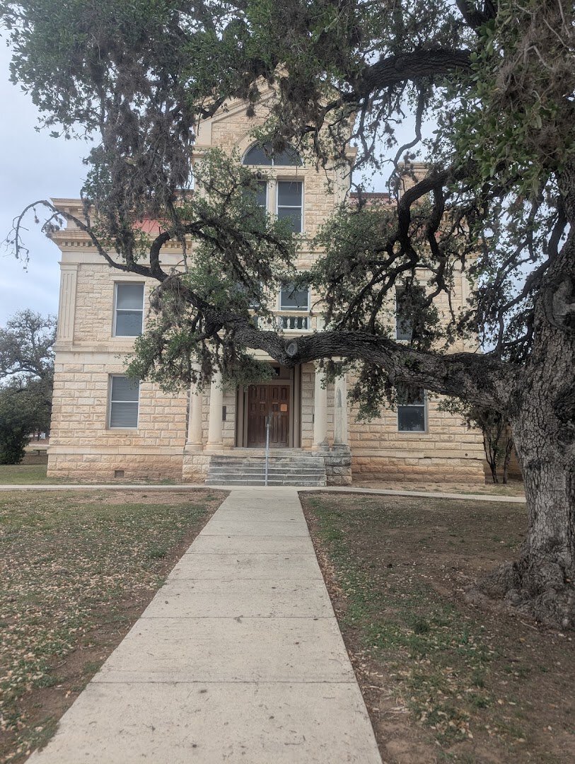 The limestone Bandera County Courthouse framed by live oaks in Bandera, Texas