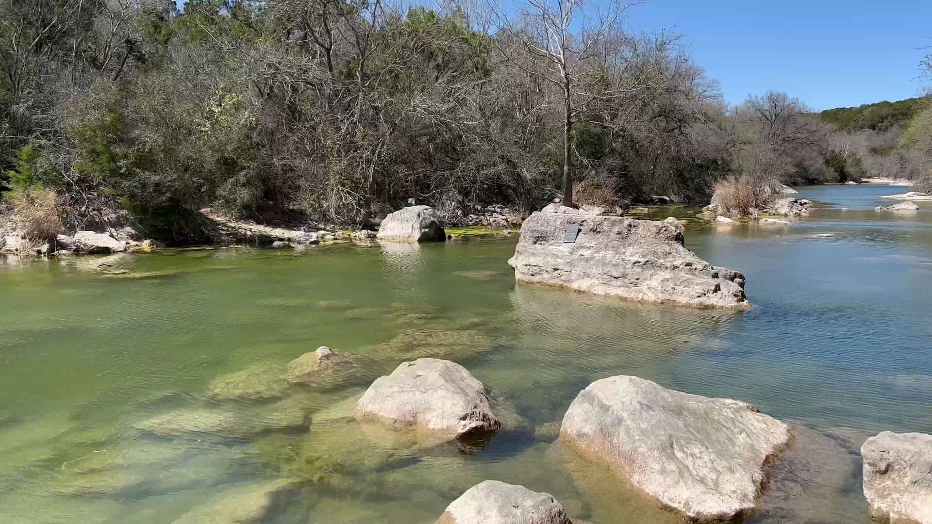Calm clear swimming hole ringed by limestone boulders on Barton Creek in Austin