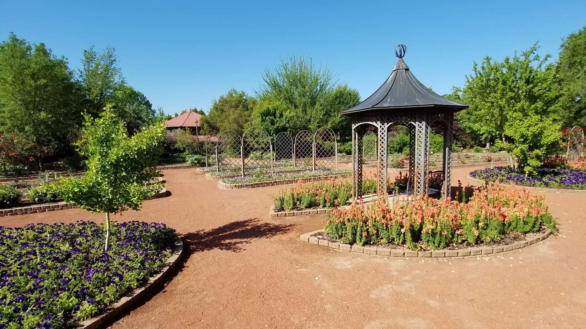 Blooming flower beds and a gazebo along a brick path at Clark Gardens in Weatherford, Texas