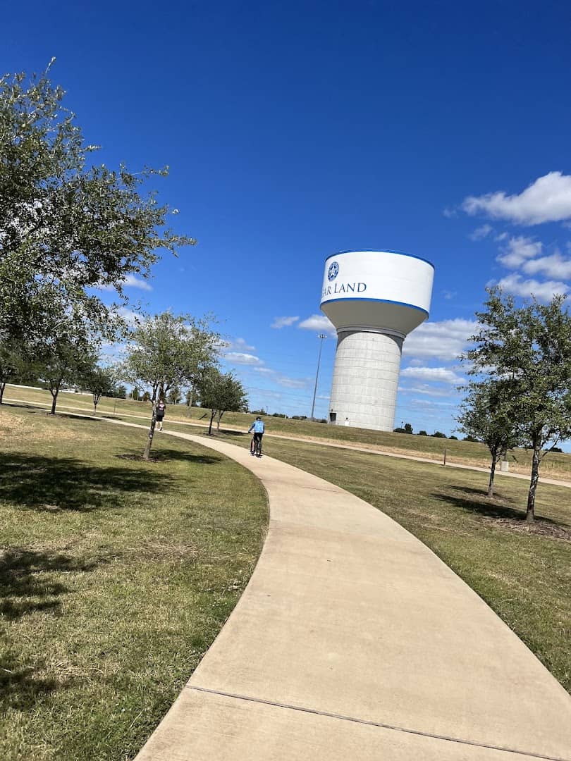 A cyclist riding the paved trail past the Sugar Land water tower at Brazos River Park