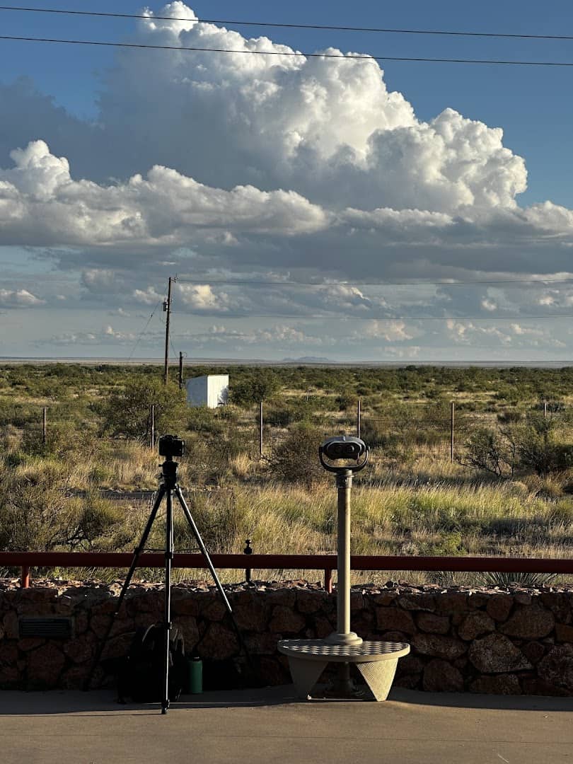 A camera on a tripod set up to watch the horizon under towering clouds near Marfa