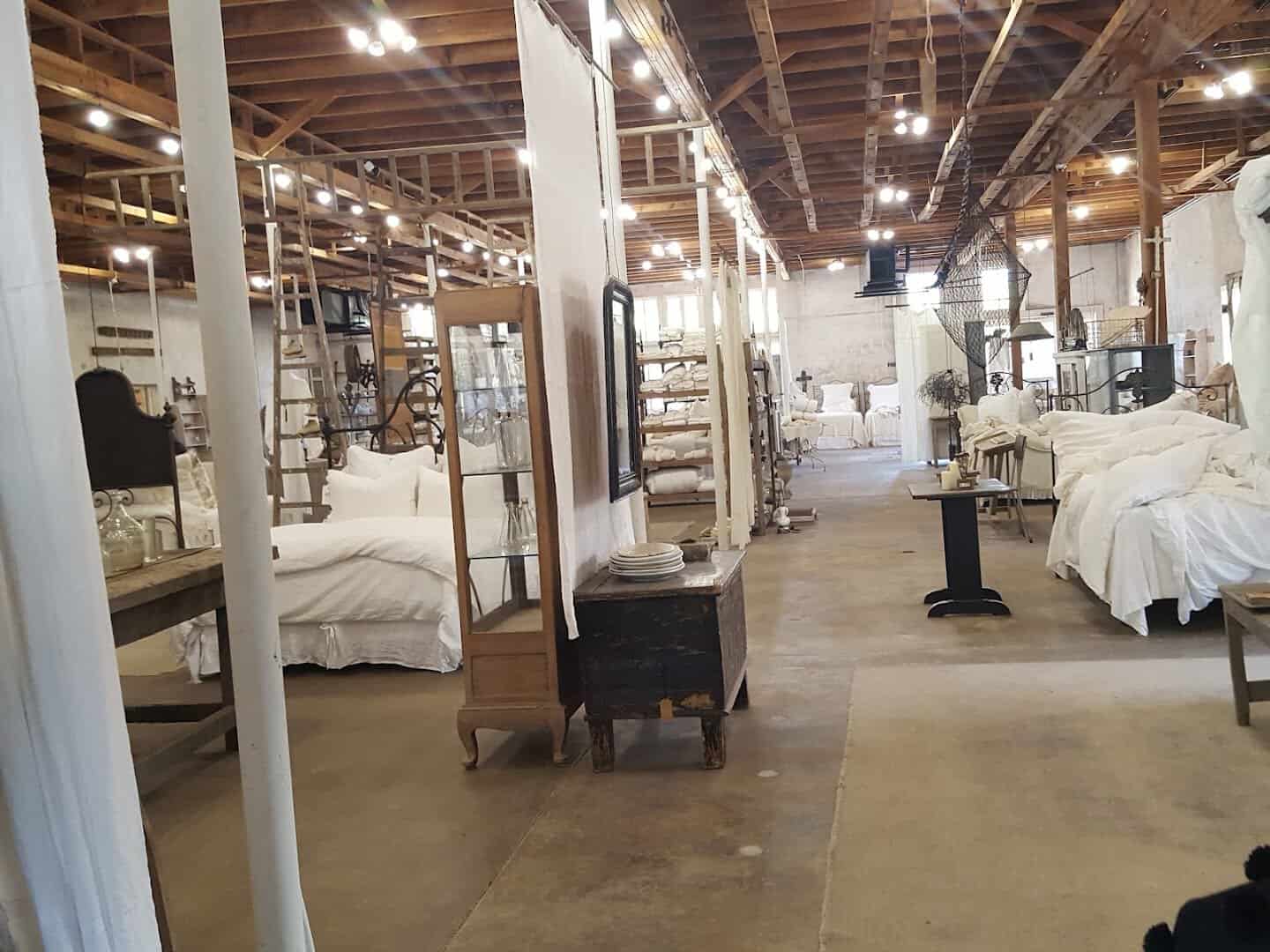 Long warehouse floor with beds, cabinets and linen displays under the rafters at Carol Hicks Bolton Antiques in Fredericksburg