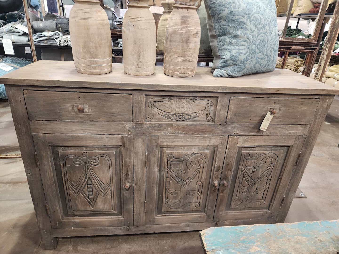 Carved antique sideboard with a price tag and stone jars on top at Carol Hicks Bolton Antiques in Fredericksburg