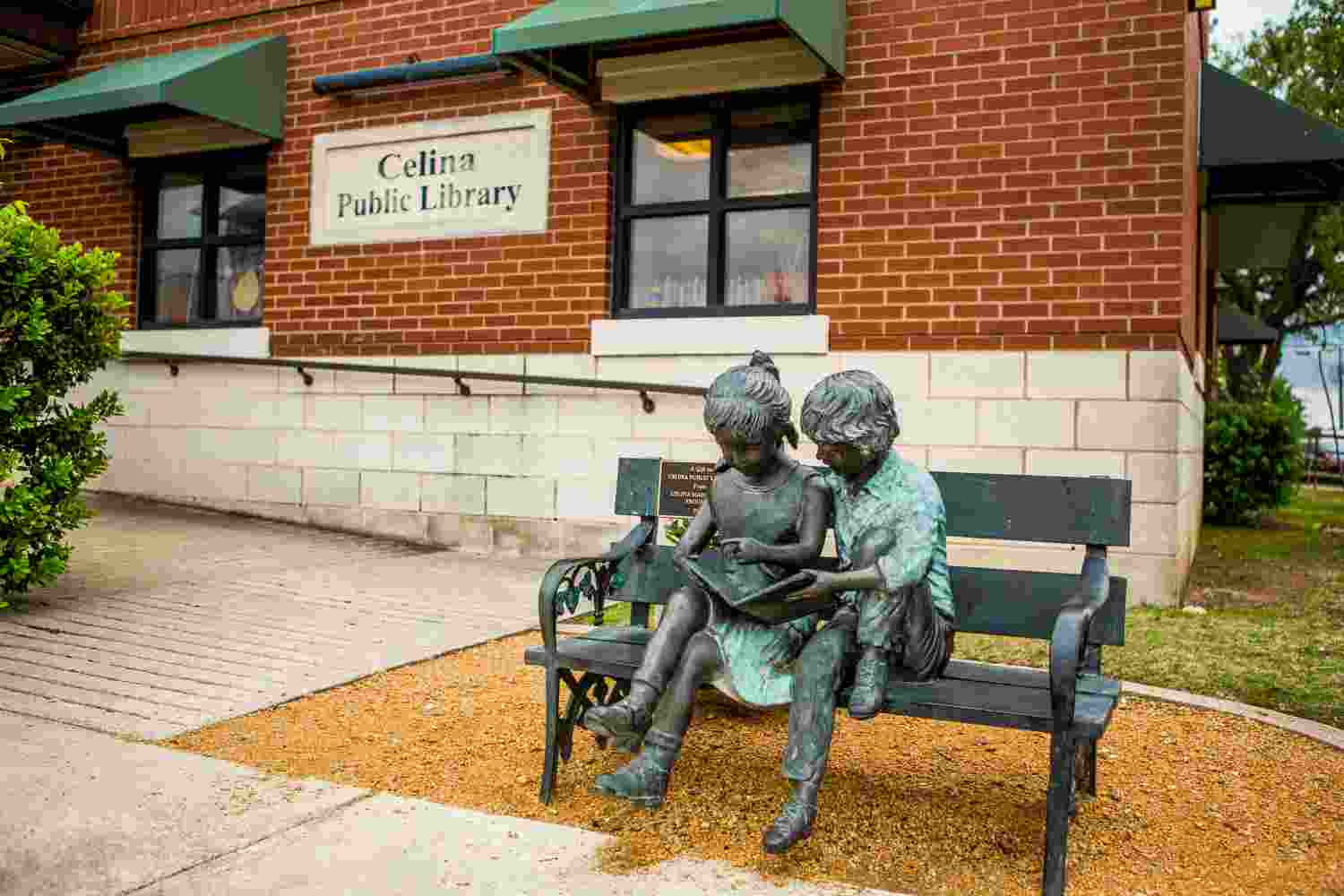 Bronze statue of two children reading on a bench outside the Celina Public Library