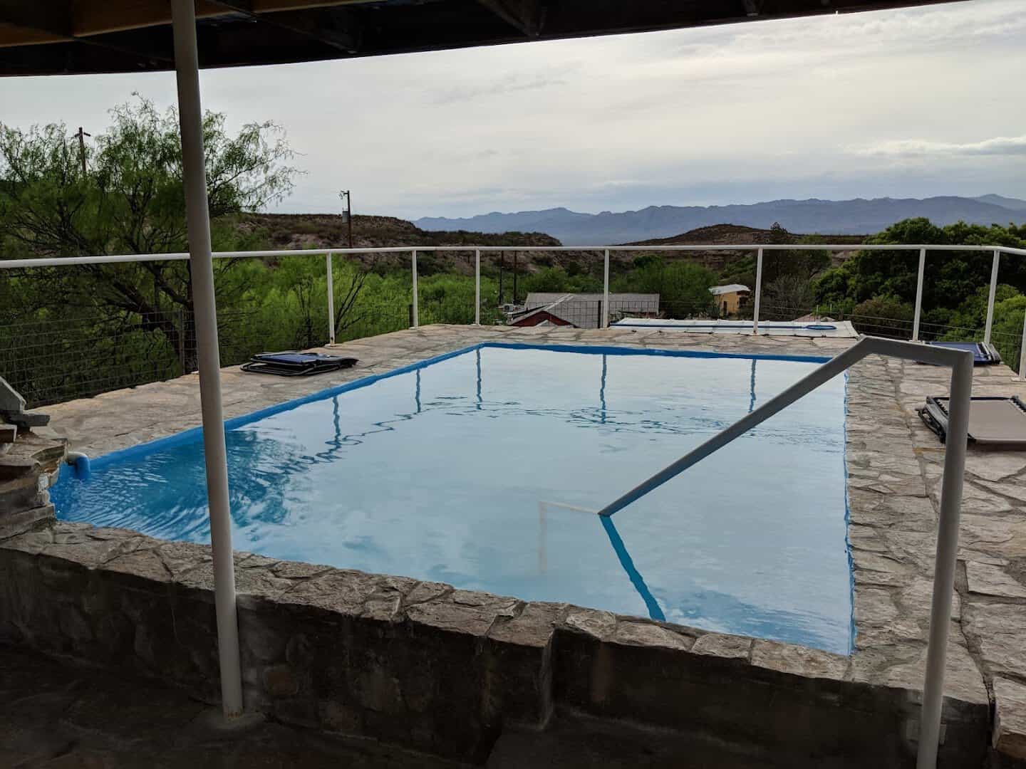 Outdoor soaking pool on a stone deck with desert hills behind at Chinati Hot Springs near Presidio, Texas